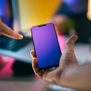 Hands pointing at a smartphone with a gradient screen in an office setting.